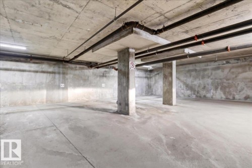 Spacious subterranean parking area featuring concrete flooring, exposed concrete walls, and concrete support pillars - 701 9707 105 Street, Edmonton, AB - Indoor Photo Showing Garage