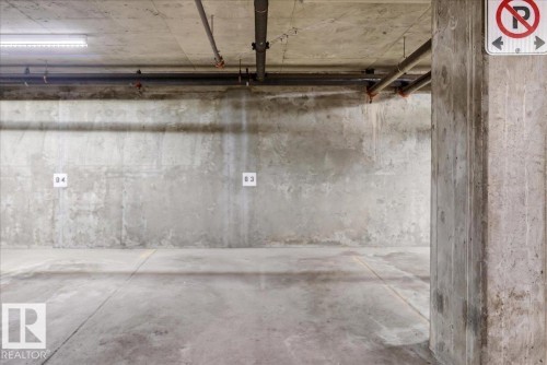 Concrete-finished parking space with exposed ceiling pipes and fluorescent lighting - 701 9707 105 Street, Edmonton, AB - Indoor Photo Showing Garage