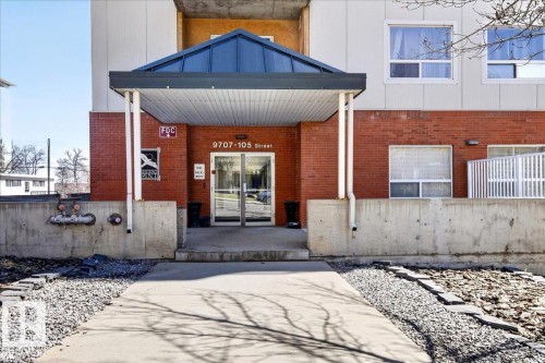 Building entrance featuring a covered walkway, glass double doors, brick siding, and a concrete foundation - 701 9707 105 Street, Edmonton, AB - Outdoor With Exterior