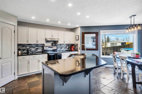 Spacious kitchen featuring an island with a built-in sink, dark countertops, white cabinetry, a patterned tile backsplash, and recessed lighting - 96 Bonin Crescent, Beaumont, AB - Indoor Photo Showing Kitchen With Upgraded Kitchen