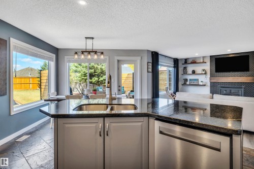 Kitchen island featuring a double basin stainless steel sink, granite countertop, and light gray cabinetry - 96 Bonin Crescent, Beaumont, AB - Indoor Photo Showing Kitchen With Fireplace With Double Sink