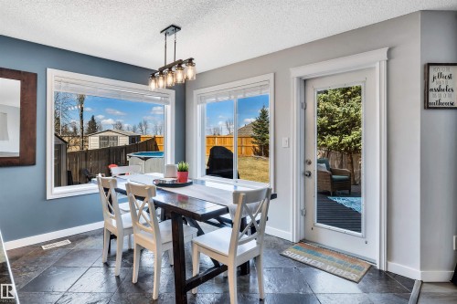 Dining area featuring large windows, a full-lite exterior door, dark square tile flooring, and an industrial-style chandelier - 96 Bonin Crescent, Beaumont, AB - Indoor Photo Showing Dining Room
