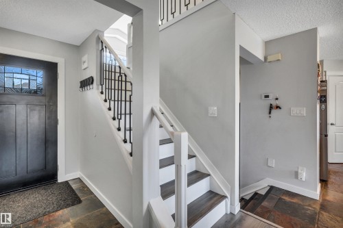 Entryway featuring slate tile flooring, a dark wood-paneled door with decorative glass inserts, and a staircase with white risers and dark wood-finish treads - 96 Bonin Crescent, Beaumont, AB - Indoor Photo Showing Other Room