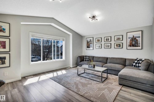 Spacious living area featuring vaulted ceilings, wood-finish flooring, a large multi-pane window, and recessed lighting - 96 Bonin Crescent, Beaumont, AB - Indoor Photo Showing Living Room