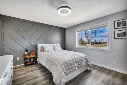 Feature wall with geometric paneling, wood-finish flooring, white trim, and a window framing outdoor scenery - 96 Bonin Crescent, Beaumont, AB - Indoor Photo Showing Bedroom