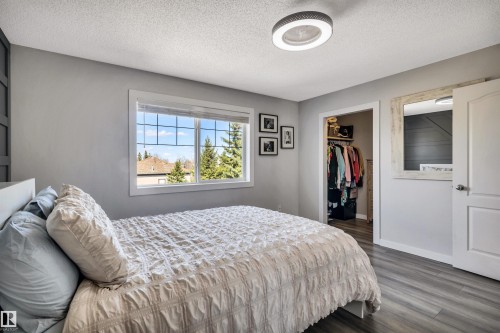 Spacious room featuring wood-finish flooring, a contemporary ceiling light fixture, a large window, and an open closet with built-in shelving - 96 Bonin Crescent, Beaumont, AB - Indoor Photo Showing Bedroom