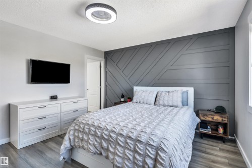 Bedroom featuring a geometric accent wall, wood-finish flooring, and a modern ceiling light fixture - 96 Bonin Crescent, Beaumont, AB - Indoor Photo Showing Bedroom