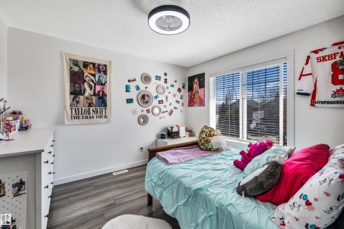 Bedroom featuring a large window with horizontal blinds, wood-finish flooring, and a ceiling-mounted light fixture - 96 Bonin Crescent, Beaumont, AB - Indoor Photo Showing Bedroom