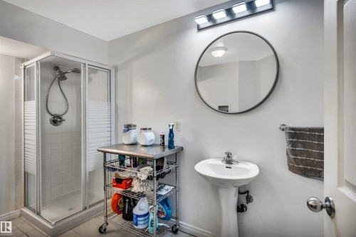 Bathroom featuring a glass-enclosed shower with white tiled walls, a pedestal sink with chrome faucet, and a circular wall-mounted mirror - 96 Bonin Crescent, Beaumont, AB - Indoor Photo Showing Bathroom