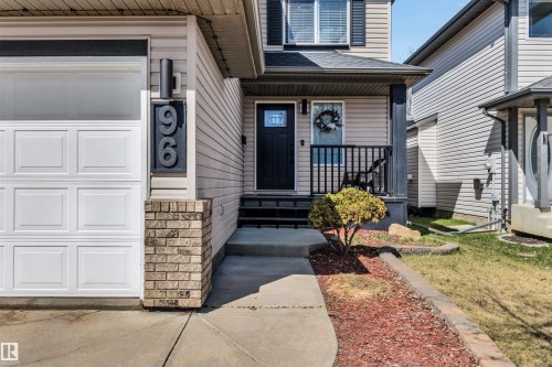 Exterior featuring light-colored siding, a white panel garage door, and a black front door with a glass insert - 96 Bonin Crescent, Beaumont, AB - Outdoor With Facade