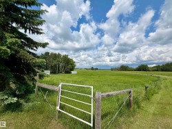 Expansive green pastureland with a partial wooden fence and white metal gate - 