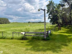 Expansive grassy field with a wooden fence line and mature trees bordering the property - 