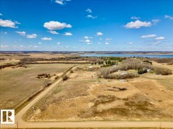 Expansive aerial landscape featuring a large body of water, broad fields, scattered clusters of trees, and a visible road - 