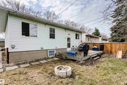 Rear exterior featuring light-colored siding, a wooden deck, and a fire pit area - 9760 64 Avenue, Edmonton, AB - Outdoor With Exterior
