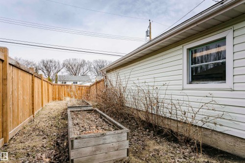 Side yard featuring a wood privacy fence, two raised garden beds, vinyl siding exterior, and a white-framed window - 9760 64 Avenue, Edmonton, AB - Outdoor