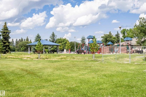Expansive green space featuring a chain-link fence, mature trees, and a distant playground - 9760 64 Avenue, Edmonton, AB - Outdoor With View