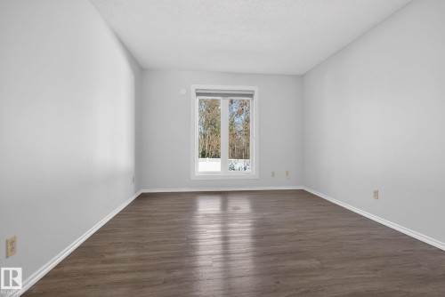 Spacious interior room featuring wood-finish flooring, light grey walls, white trim, and a prominent window - 46 903 109 Street, Edmonton, AB - Indoor Photo Showing Other Room