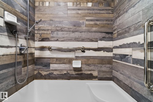 Shower enclosure featuring distressed wood-look tile, a handheld shower fixture, integrated grab bars, and a white tub basin - 46 903 109 Street, Edmonton, AB - Indoor Photo Showing Bathroom