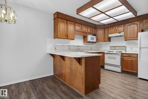 Kitchen featuring wood-finish cabinetry, light-toned countertops, white subway tile backsplash, and wood-finish flooring - 46 903 109 Street, Edmonton, AB - Indoor Photo Showing Kitchen