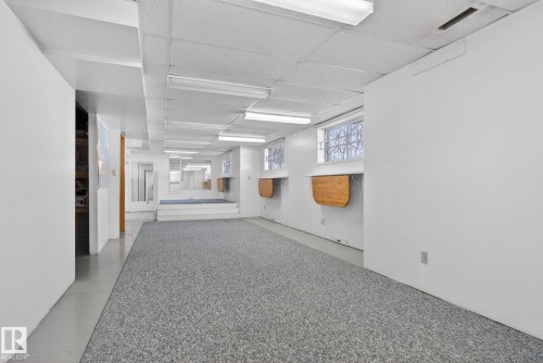 Lower level featuring textured carpeting, white painted walls, dropped ceiling with integrated lighting, built-in elevated platform, and window wells with wood-finish shelving - 46 903 109 Street, Edmonton, AB - Indoor Photo Showing Other Room