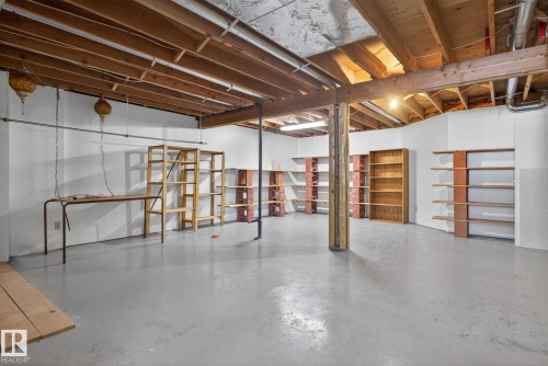Expansive utility space featuring painted concrete flooring, exposed ceiling joists, white painted walls, and multiple built-in shelving units - 46 903 109 Street, Edmonton, AB - Indoor Photo Showing Basement