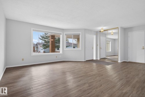 Spacious room featuring wood-finish flooring, light grey painted walls, and ample natural light from multiple windows - 46 903 109 Street, Edmonton, AB - Indoor Photo Showing Living Room