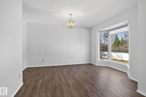 Spacious room featuring wood-finish flooring, a bay window with multiple panes, a brass-toned chandelier, and white baseboards - 46 903 109 Street, Edmonton, AB - Indoor Photo Showing Other Room