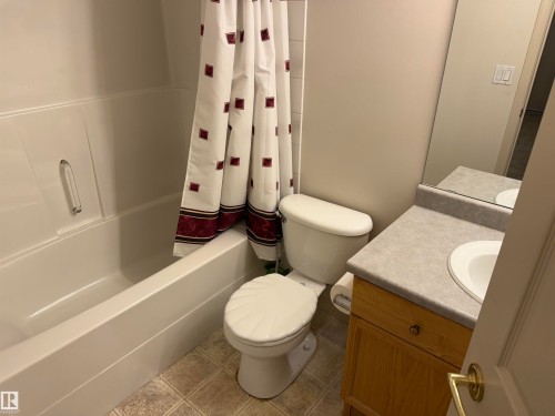 Bathroom featuring a white tub and shower combination, a toilet, a light wood-finish vanity with a built-in sink, a light-toned countertop, and a wall-mounted mirror - 14 330 Galbraith Close, Edmonton, AB - Indoor Photo Showing Bathroom