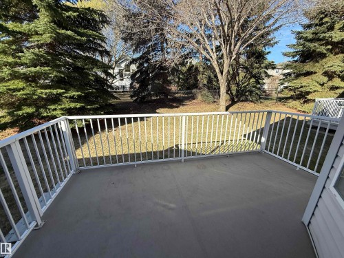 Spacious outdoor deck featuring a gray surface and white railing, overlooking a grassy area with mature evergreen trees and deciduous trees - 14 330 Galbraith Close, Edmonton, AB - Outdoor