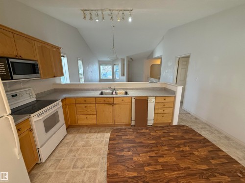 Kitchen featuring wood cabinetry, laminate countertops, and a white electric range - 14 330 Galbraith Close, Edmonton, AB - Indoor Photo Showing Kitchen With Double Sink