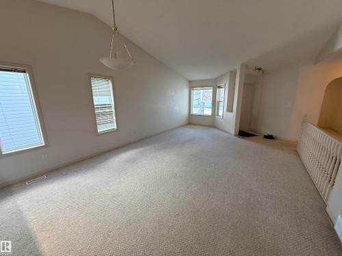 Spacious room featuring vaulted ceilings, light-toned carpeting, multiple windows with blinds, a bay window configuration, and a decorative spindle railing - 14 330 Galbraith Close, Edmonton, AB - Indoor Photo Showing Other Room