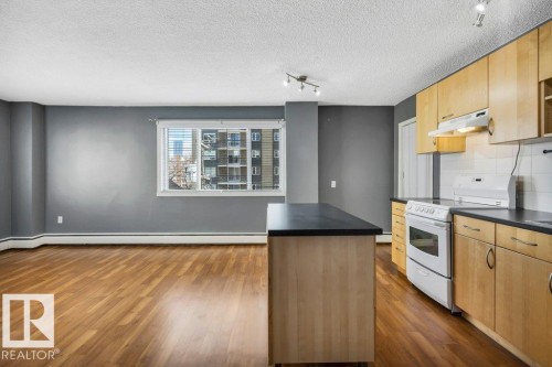 Kitchen featuring wood-finish cabinetry, white appliances, and a central island with a dark countertop - 403 10021 116 Street, Edmonton, AB - Indoor Photo Showing Kitchen