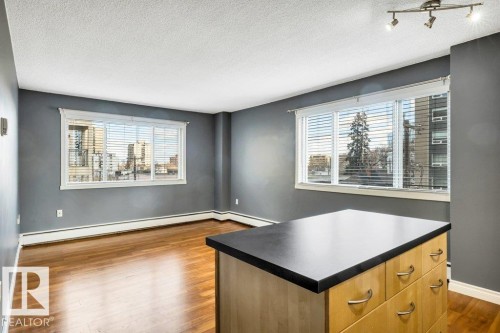 Open-concept living area featuring wood-finish flooring and two large windows with horizontal blinds - 403 10021 116 Street, Edmonton, AB - Indoor Photo Showing Other Room