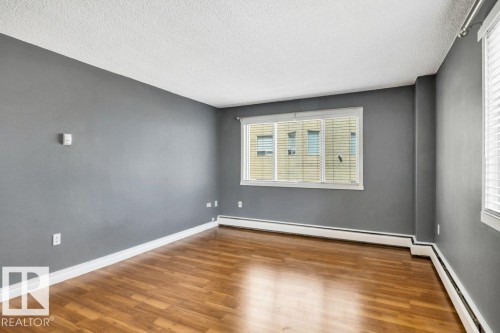 Spacious room featuring wood-finish flooring, neutral gray walls, and large windows with blinds - 403 10021 116 Street, Edmonton, AB - Indoor Photo Showing Other Room