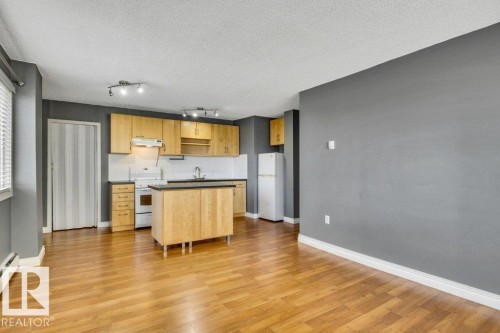 Open-concept kitchen featuring wood-finish flooring, light wood cabinetry, white tile backsplash, and a central island with a dark countertop - 403 10021 116 Street, Edmonton, AB - Indoor Photo Showing Kitchen
