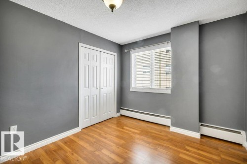 Room featuring wood-finish flooring, a double bi-fold closet, baseboard heating, a single window with blinds, and an overhead light fixture - 403 10021 116 Street, Edmonton, AB - Indoor Photo Showing Other Room