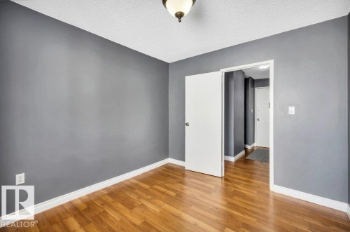 Room featuring wood-finish flooring, neutral gray wall tones, and white baseboards - 403 10021 116 Street, Edmonton, AB - Indoor Photo Showing Other Room