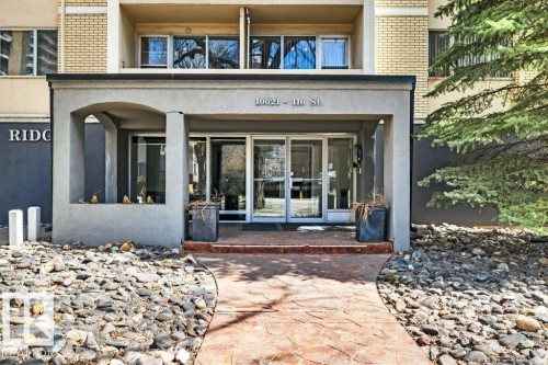 Building entrance featuring a stamped concrete pathway, glass double doors, a concrete archway, and rock landscaping - 403 10021 116 Street, Edmonton, AB - Outdoor