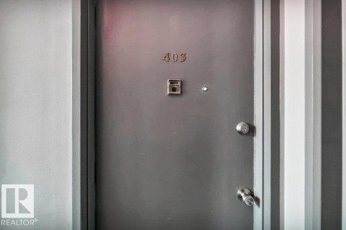 Solid gray entry door featuring a door knocker, peephole, and polished chrome hardware - 403 10021 116 Street, Edmonton, AB - Indoor