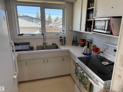 Functional kitchen featuring white cabinetry, a double basin stainless steel sink with a high-arc faucet, white laminate countertops, and a white electric range - 16112 87 Avenue, Edmonton, AB - Indoor Photo Showing Kitchen With Double Sink