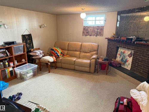 Carpeted living space featuring a brick fireplace with a dark-toned hearth, light wood-finish wall paneling, and a window with a security bar - 16112 87 Avenue, Edmonton, AB - Indoor Photo Showing Living Room