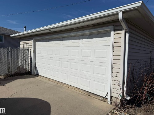 Detached garage featuring a paneled white garage door, light-colored vinyl siding, and concrete driveway - 16112 87 Avenue, Edmonton, AB - Outdoor