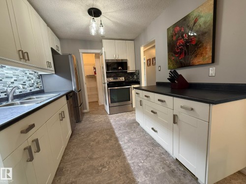 Modern kitchen featuring white shaker cabinetry with brushed nickel hardware, dark countertops, and a mosaic tile backsplash - 5 2204 118 Street, Edmonton, AB - Indoor Photo Showing Kitchen With Double Sink