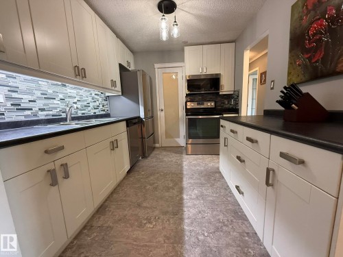 Kitchen featuring white shaker-style cabinetry with brushed nickel hardware, black countertops, and a gray-toned mosaic tile backsplash - 5 2204 118 Street, Edmonton, AB - Indoor Photo Showing Kitchen With Double Sink