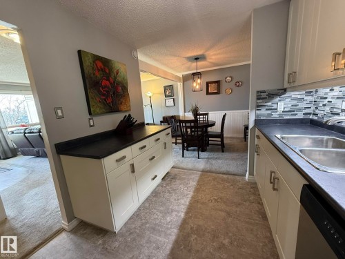 Kitchen featuring light cabinetry, dark countertops, a mosaic tile backsplash, and a double basin sink - 5 2204 118 Street, Edmonton, AB - Indoor Photo Showing Kitchen With Double Sink