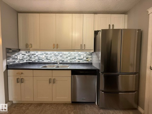 Contemporary kitchen featuring light-toned cabinetry, a mosaic tile backsplash, dark countertops, a double basin stainless steel sink with a chrome faucet, and wood-finish flooring - 5 2204 118 Street, Edmonton, AB - Indoor Photo Showing Kitchen With Double Sink
