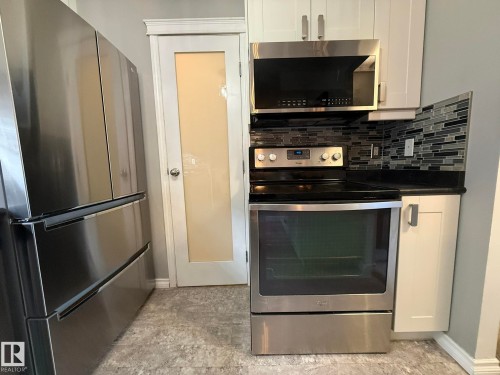 Modern kitchen featuring stainless steel appliances, black countertops, a mosaic tile backsplash, white shaker-style cabinetry, and wood-finish flooring - 5 2204 118 Street, Edmonton, AB - Indoor Photo Showing Kitchen With Upgraded Kitchen