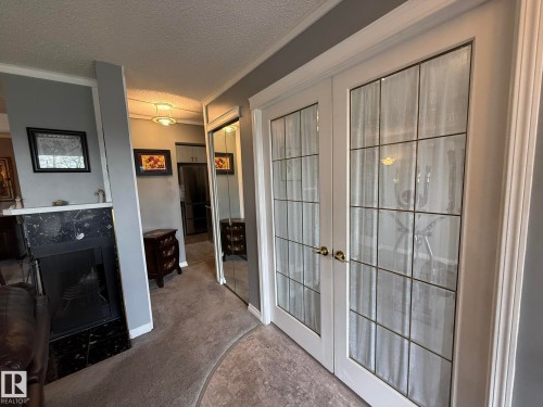 White French doors with frosted glass panels, brass hardware, gray wall tones, crown molding, and a built-in fireplace with a black surround - 5 2204 118 Street, Edmonton, AB - Indoor Photo Showing Other Room