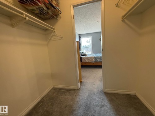 Walk-in closet with wire shelving, integrated hanging rods, white baseboards, and neutral carpeting - 5 2204 118 Street, Edmonton, AB - Indoor