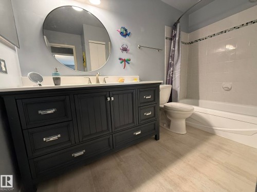 Bathroom featuring a dark wood vanity with ample storage, a white countertop, and a circular wall-mounted mirror - 5 2204 118 Street, Edmonton, AB - Indoor Photo Showing Bathroom